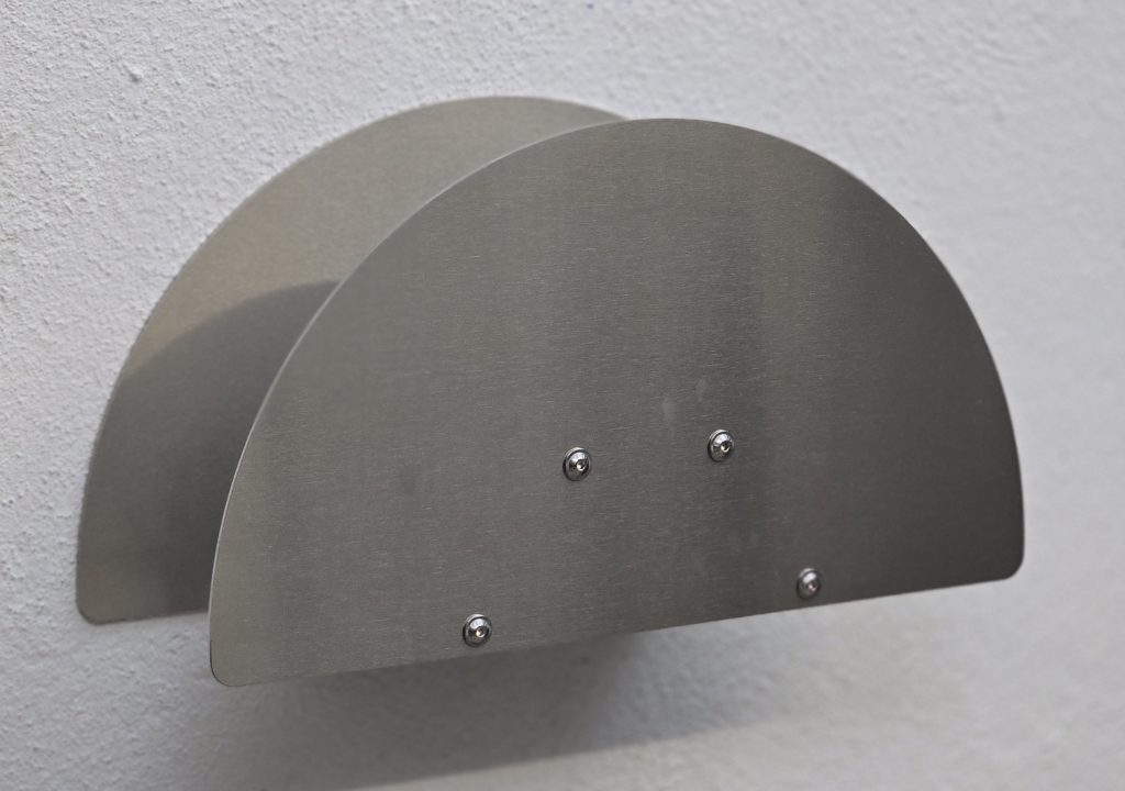 Standard-Frontblende Schrägansicht der Standard-Frontblende eines Edelstahl-Schlauchhalters mit sichtbaren Schraubenköpfen.